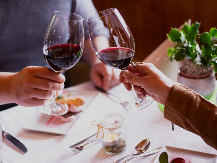 Paar stößt mit Rotwein an, weiß gedeckter Tisch mit Kerzenlicht in holzvertäfelter Stube