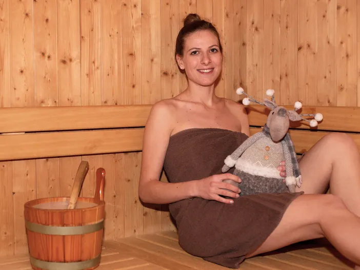 Lächelnde Frau in Handtuch in der Zirbensauna mit Holzkübel und dekorativen Details
